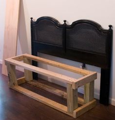 a wooden bench sitting next to a black headboard on top of a hard wood floor