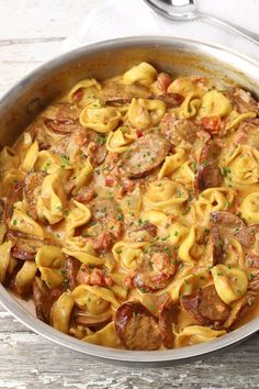 a pan filled with pasta and sausage on top of a wooden table