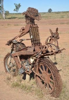 a rusted out motorcycle sitting in the middle of a field with an animal sculpture on it's back