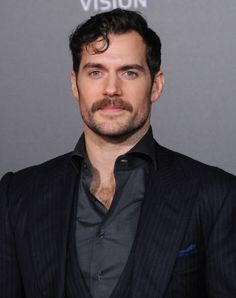 a man in a suit and tie poses for the camera on a red carpet at an event