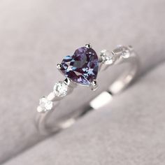 a heart shaped purple diamond ring with three diamonds on the band and side stones around it