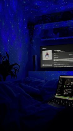 a laptop computer sitting on top of a bed in front of a tv screen with blue lights