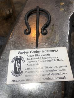 an iron hook is sitting on top of a piece of metal with a business card attached to it