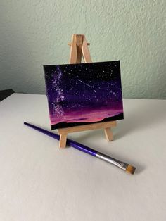 an easel with a purple and black painting on it next to a paintbrush