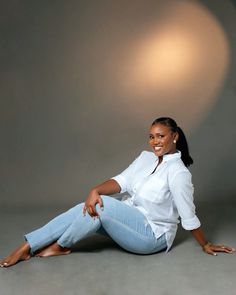 a woman is sitting on the floor posing for a photo in jeans and a white shirt