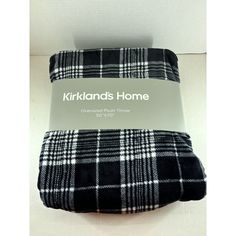 the black and white plaid blanket is folded on top of a cardboard box with an ad for kirklands home