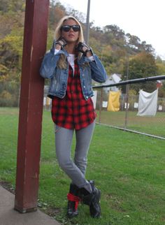 a woman in plaid shirt and jean jacket leaning on pole