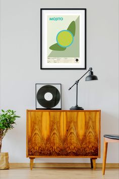 an art print hangs on the wall next to a sideboard with a lamp and potted plant