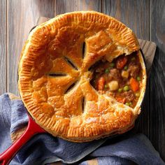 a pie with meat and vegetables in it sitting on a wooden table next to a blue towel