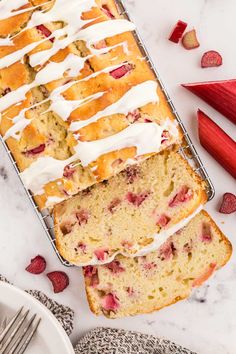 two slices of strawberry bread with icing and strawberries next to them on a white surface