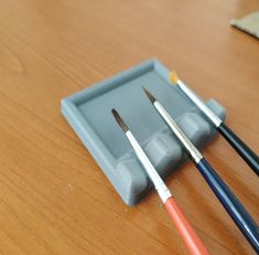 three paintbrushes sitting on top of a wooden table next to an empty tray