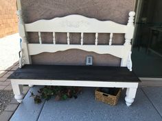 a white bench sitting on top of a sidewalk next to a building with a basket