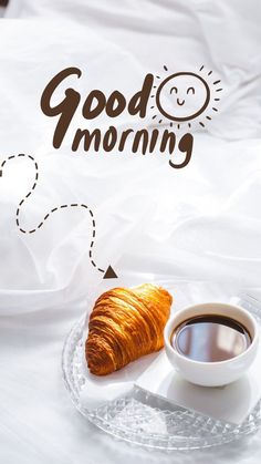 a cup of coffee and croissant on a plate with the words good morning above it