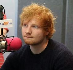 a man with red hair is sitting in front of a microphone and looking at the camera