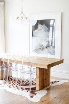 a dining room table with clear chairs and a painting on the wall in the background