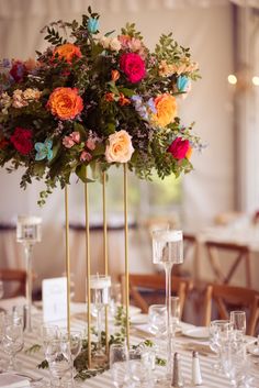 an arrangement of flowers in tall gold vases on a table with place cards and wine glasses