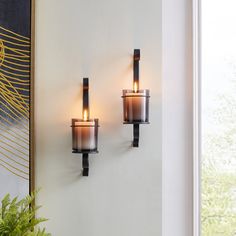 two candles are lit on the wall next to a potted plant