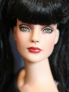 a close up of a doll with long black hair and green eyes wearing red lipstick