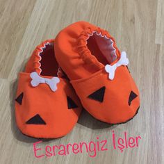 an orange pair of baby shoes with black and white bows on the toes, sitting on a wooden floor