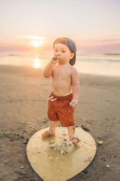 a young boy standing on top of a surfboard in the sand at the beach