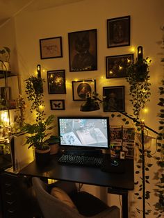 a desk with a computer on it in front of some plants and framed pictures hanging on the wall