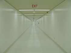 an exit sign is in the middle of a long hallway with white walls and floors