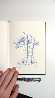 a hand is holding an open book in front of a drawing of a tree and its branches