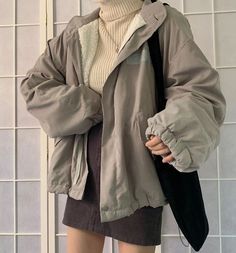 a woman standing in front of a white tiled wall wearing a gray jacket and hat