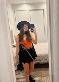 a woman in an orange shirt and black skirt taking a selfie with her cell phone