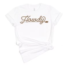 Howdy t-shirt for country girls and cowgirls is a Next Level brand tee and comes in unisex cut and sizes. This graphic tee features the popular rope font Howdy with a rustic arrow underscore. A vintage style graphic for the modern cowgirl. Looks perfect alone or layered under a chic blazer for a more sophisticated look. The perfect shirt for the rodeo, country music concert, a bachelorette party in Nashville or around town. Our graphic tees are super soft and super comfy! Unisex sizing. This uni Fall Graphic Print T-shirt For Country Events, Country Style White Graphic T-shirt, White Letter Print T-shirt For Ranch, Fall Country Events Short Sleeve T-shirt, Graphic Tee For Western-themed Fall Events, Short Sleeve T-shirt For Country Events, Bachelorette Party In Nashville, Rope Font, Country Music Concert