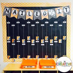 an orange and black classroom desk with yellow bins on it, next to a bulletin board that says nailed out