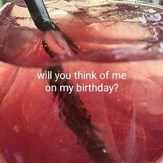 a glass filled with liquid sitting on top of a table next to a sign that says, will you think of me on my birthday?