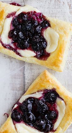 four small pastries on a white plate covered in jam and jelly toppings, with sauce drizzled over the top