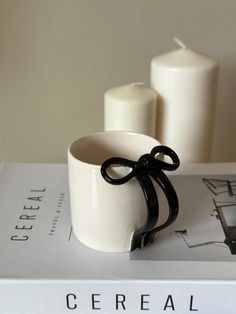 a white cup sitting on top of a book next to two candle holders with black ribbon