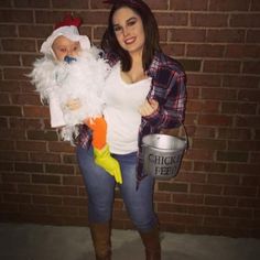 a woman holding a baby in her arms while standing next to a brick wall with a chicken costume on