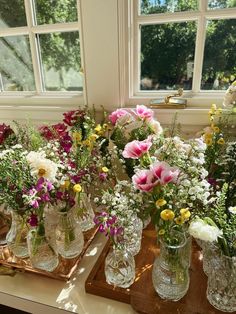 several vases filled with different types of flowers on top of a wooden table in front of a window