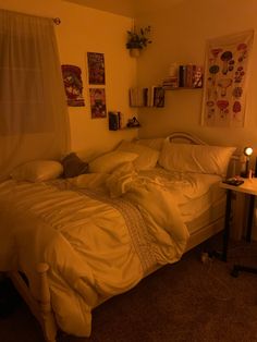 an unmade bed in a dimly lit room with pictures on the wall above it