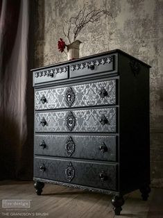 an ornate black dresser with flowers in a vase on top