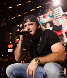 a man sitting on the ground while holding a microphone in his hand and wearing a hat