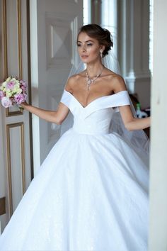 a woman in a white wedding dress holding a bouquet and looking at the camera while standing next to an open door