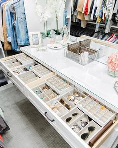 a white table topped with lots of drawers filled with rings and bracelets next to a mirror