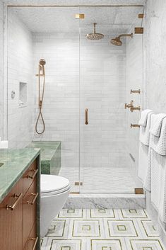 a bathroom with marble counter tops and gold fixtures on the shower wall, along with a green tiled floor