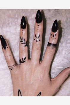 a woman's hand with black nail polish and tattoos on her fingers, which are decorated with leaves