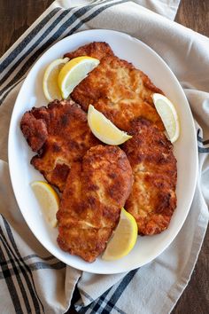 two pieces of fried fish on a plate with lemon wedges