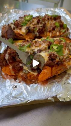 a pizza with cheese and other toppings on it sitting on tin foil next to a knife