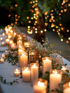 many lit candles are lined up on a table with greenery and flowers in front of them