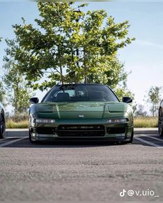 two green sports cars parked next to each other in a parking lot with trees behind them