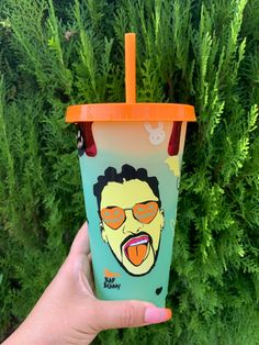 a hand holding up a plastic cup with an image of a man wearing sunglasses on it