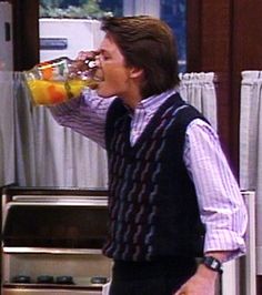 a man drinking out of a glass while standing in front of an oven