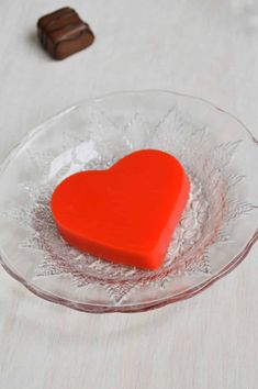 a red heart in a glass bowl on a table next to two chocolates and a candy bar